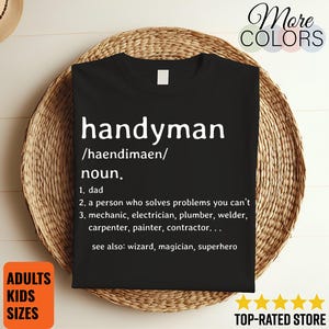 Könnte beinhalten: Schwarzes T-Shirt mit dem weißen Wort "handyman", seiner phonetischen Aussprache und Definition. Die Definition beinhaltet "Papa" und "eine Person, die Probleme löst, die Sie nicht können". Das T-Shirt liegt auf einem geflochtenen Korb.
