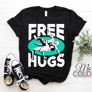 May include: Black t-shirt with white text that says "FREE HUGS" and a graphic of two wrestlers in a green circle.