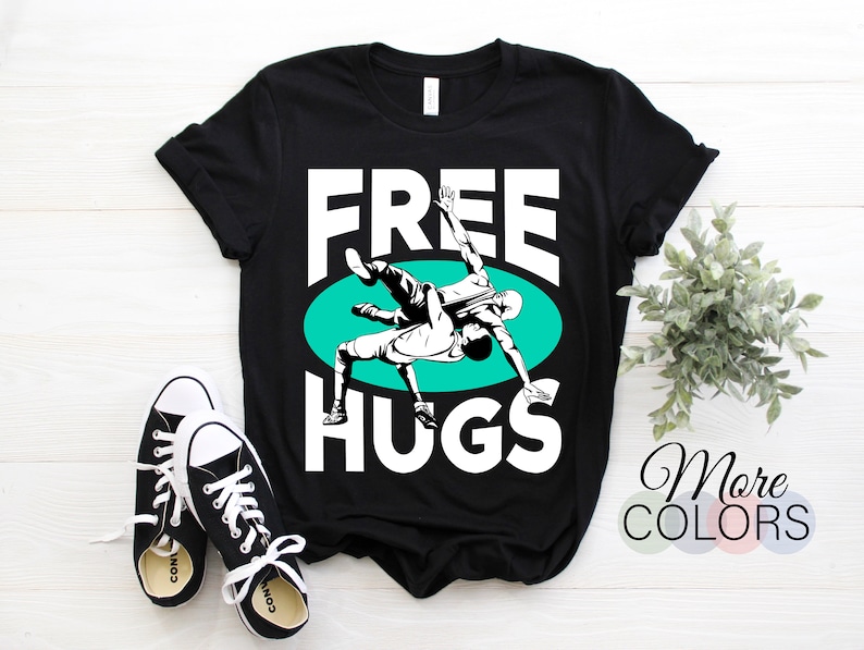 May include: Black t-shirt with white text that says "FREE HUGS" and a graphic of two wrestlers in a green circle.