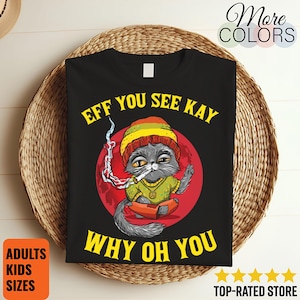 May include: Black t-shirt with a graphic of a gray cat wearing a Rasta hat and smoking a cigarette, set against a red circle. The text "EFF YOU SEE KAY WHY OH YOU" is in yellow.