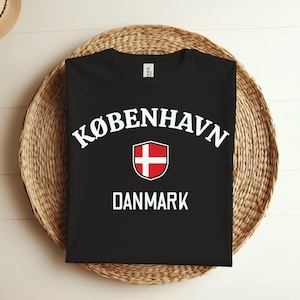 May include: Black t-shirt with white text that reads "KØBENHAVN DANMARK" and a red and white Danish flag in a shield.