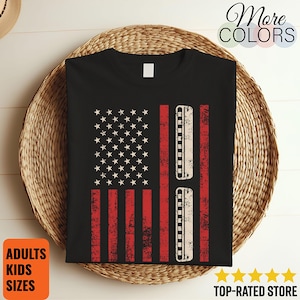 May include: Black t-shirt featuring a distressed American flag design with red stripes and white stars. The flag's stripes are replaced with harmonica illustrations. The shirt has the text "More Colors", "Adults Kids Sizes", and "Top-Rated Store".
