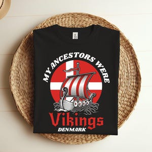 May include: Black t-shirt featuring a white graphic of a Viking ship sailing under the Danish flag. The text "My ancestors were Vikings Denmark" is printed on the shirt.