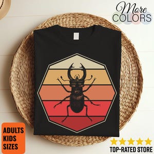Peut inclure: T-shirt noir avec une illustration rétro d'un lucane cerf-volant dans un design géométrique à rayures orange, rouge et beige. Le t-shirt porte les mentions "More Colors" et "Adults Kids Sizes".
