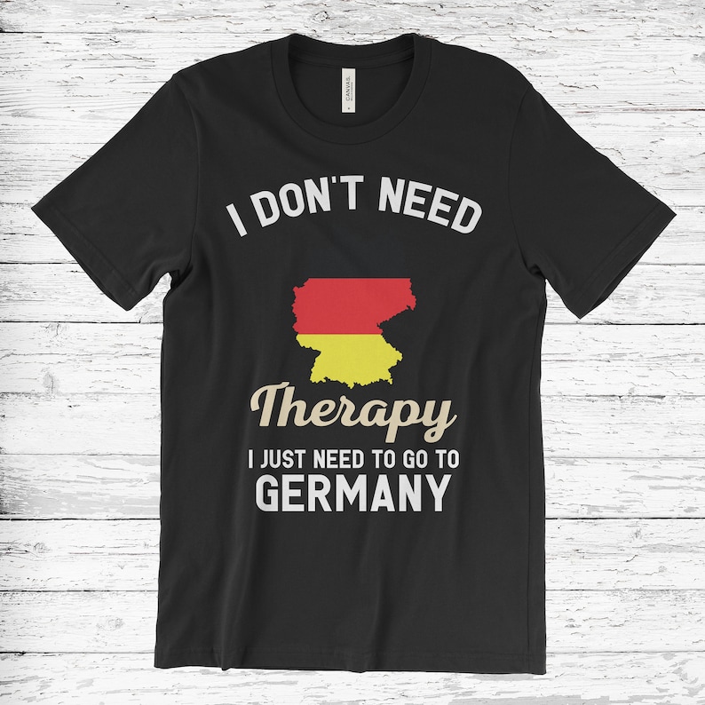 May include: Black t-shirt with the text "I DON'T NEED THERAPY I JUST NEED TO GO TO GERMANY." The shirt features a graphic of the German flag in the shape of the country. The text and graphic are in white and the German flag is red, yellow, and black.