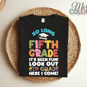 Op de afbeelding: Zwart T-shirt met kleurrijke tekst die luidt: "SO LONG FIFTH GRADE" en "IT'S BEEN FUN! LOOK OUT 6TH GRADE HERE I COME!". Een afstudeerhoed-afbeelding staat boven de woorden "FIFTH GRADE".