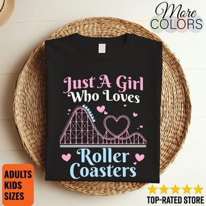 Puede incluir: Una camiseta negra con un gráfico de una montaña rusa rosa que forma un corazón. El texto Just A Girl Who Loves Roller Coasters aparece en letras rosas y azul claro, decorado con pequeños corazones rosas y un vagón de montaña rusa.