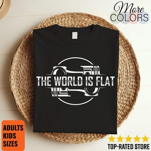 May include: Black t-shirt with a white graphic design featuring the text "THE WORLD IS FLAT" inside a circle with a piston design. The shirt is displayed on a woven basket.
