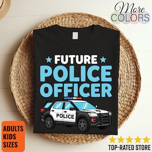 Puede incluir: Una camiseta negra con el texto FUTURE POLICE OFFICER en letras azul claro y dos estrellas azul claro. Debajo del texto hay una ilustración gráfica de un vehículo policial SUV en blanco y negro con luces rojas y azules en el techo.