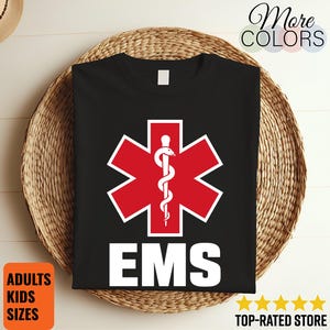 May include: A black t-shirt featuring a red six-pointed Star of Life symbol with a white serpent and staff emblem in the centre. Below the graphic, the letters EMS are printed in large, bold, white capital letters on the front of the shirt.
