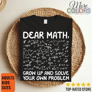 May include: Black t-shirt with white text and mathematical equations. The text says "DEAR MATH, GROW UP AND SOLVE YOUR OWN PROBLEM." The shirt is displayed on a woven basket. Additional text includes "ADULTS KIDS SIZES" and "TOP-RATED STORE."