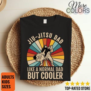 May include: Black t-shirt with a Jiu-Jitsu graphic. The design features two figures in a martial arts pose set against a retro rainbow circle. Text reads "Jiu-Jitsu Dad Like a Normal Dad But Cooler". Includes "Adults Kids Sizes" and "Top-Rated Store" text.