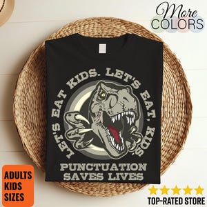 May include: Black t-shirt with a dinosaur graphic and the text "LET'S EAT KIDS. LET'S EAT, KIDS. PUNCTUATION SAVES LIVES." The shirt is displayed on a woven basket. The shirt is available in adult and kids sizes.