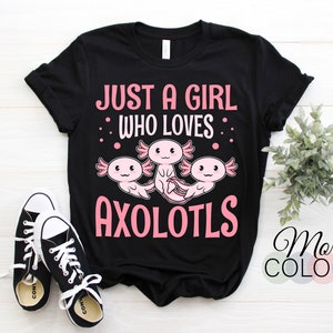 Könnte beinhalten: Schwarzes T-Shirt mit rosa Schriftzug "Just a girl who loves axolotls". Drei Axolotl-Cartoons sind in rosa dargestellt. Der Text "More Colors" befindet sich in der rechten unteren Ecke des Bildes.