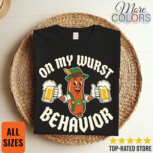 Può includere: Una t-shirt nera con la grafica di una salsiccia in stile cartoon che indossa un cappello verde con piuma e lederhosen, mentre tiene in mano due boccali di birra. Il testo "ON MY WURST BEHAVIOR" è stampato in maiuscolo bianco attorno al disegno.