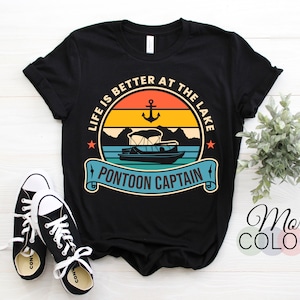 Op de afbeelding: Zwart T-shirt met een vintage-stijl grafische afbeelding met de tekst "Het leven is beter aan het meer" met een pontonboot en een anker. De tekst "Pontoon Captain" staat onder de afbeelding.