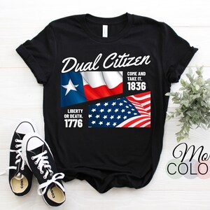 May include: Black t-shirt with the text "Dual Citizen" and the flags of Texas and the United States. The shirt also features the phrases "Come and take it. 1836" and "Liberty or death. 1776". Black and white sneakers are in the foreground.