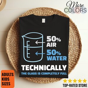 May include: Black t-shirt with a beaker graphic and the text "50% Air, 50% Water, Technically The Glass Is Completely Full." The shirt also has the words "Adults Kids Sizes" on the bottom left.