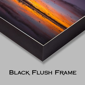 May include: A black framed canvas print of a sunset over a body of water with a flock of birds flying overhead.