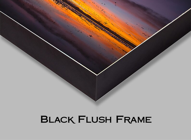 May include: A black framed canvas print of a sunset over a body of water with a flock of birds flying overhead.