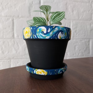 以下が含まれることがあります： フィンセント・ヴァン・ゴッホの星月夜にインスパイアされた、青と黄色のペイントデザインが施された黒いテラコッタ製のプランター。プランターには、渦巻き状のラインと黄色の星で飾られた、マッチする受け皿が付いています。
