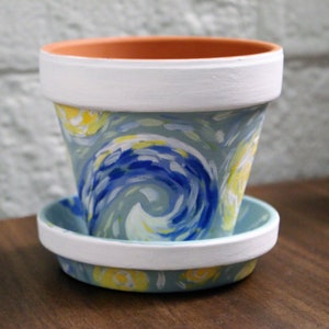 May include: A white ceramic planter with a blue and yellow swirling design, reminiscent of a famous painting. The planter has a matching saucer.