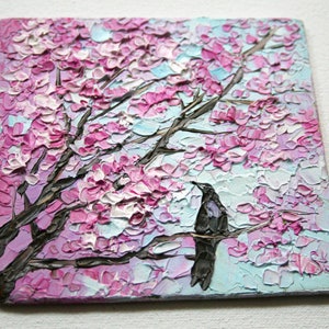 May include: A painting of a pink and white cherry blossom tree with a black bird perched on a branch. The background is a light blue sky.