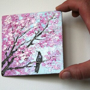 May include: A painting of a pink and white cherry blossom tree with two black birds perched on a branch. The painting is done in a textured style, giving the impression of brushstrokes.