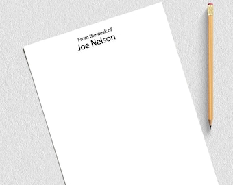 Könnte beinhalten: Ein weißes Blatt Papier mit dem Text "From the desk of Joe Nelson" oben. Ein Bleistift und Büroklammern liegen auf der Oberfläche neben dem Papier.
