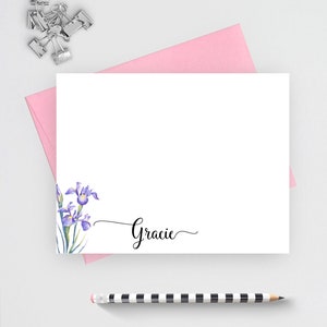 May include: A white card with a purple and green watercolor iris flower design in the bottom left corner. The name "Gracie" is written in cursive in the bottom right corner.