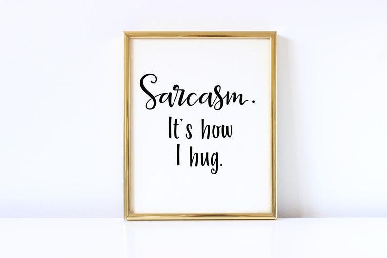 May include: A gold framed print with the text "Sarcasm. It's how I hug." in black cursive font on a white background.