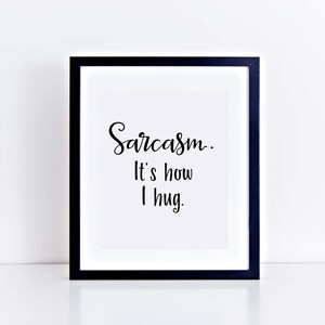 May include: A black framed print with white background and the text "Sarcasm. It's how I hug."