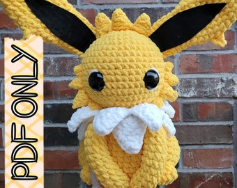 May include: A crocheted plush toy of a yellow Eevee with black ears and white fur around its neck. The toy is sitting on a brick wall.