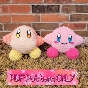 May include: Two crocheted plush toys, one pink and one peach, resembling the characters Kirby and King Dedede from the video game series Kirby. The toys are sitting on a bed of brown grass.