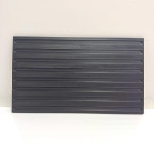 May include: A rectangular black tray featuring a series of parallel horizontal grooves across its surface. The tray has a flat, smooth border and a textured finish within the recessed channels, providing a structured and uniform appearance.