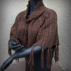 May include: A brown crocheted shawl with fringe. The shawl is draped over a mannequin.