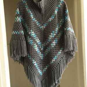 May include: Gray crochet poncho with a high neck and fringe trim. The poncho features a geometric pattern in shades of blue and white.