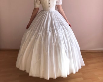 May include: A white off-the-shoulder dress with a fitted bodice and a full skirt. The dress has a lace trim and is worn with a white corset.