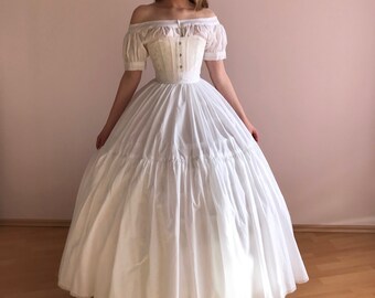 May include: A white off-the-shoulder dress with a fitted bodice and a full skirt. The dress has a lace trim and is worn with a white corset.