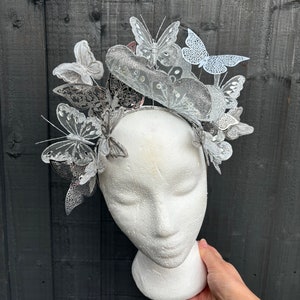 May include: A silver butterfly headband with multiple layered butterflies. The headband is on a white mannequin head.
