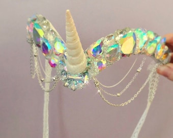 May include: A white unicorn headband with iridescent crystals and a white shell horn. The headband has silver chains hanging from it.