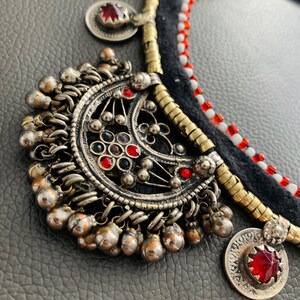 May include: A silver and gold necklace with red and white beads, a large silver pendant with a crescent moon design, and several smaller silver pendants with red stones.
