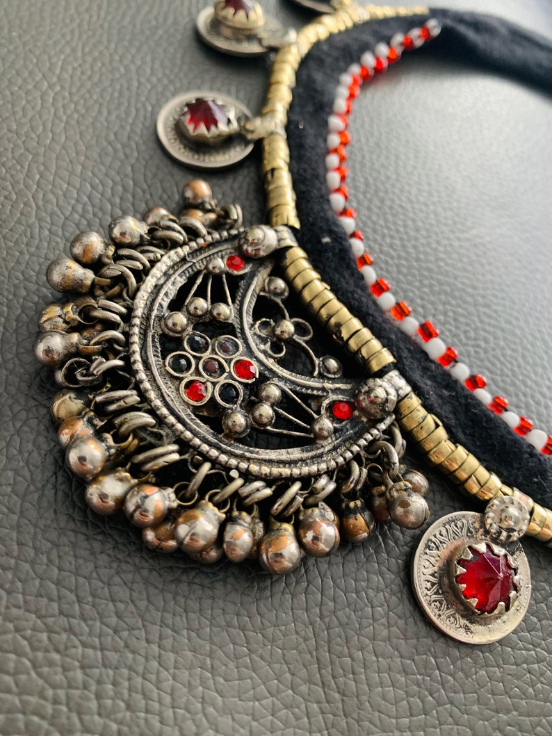 May include: A silver and gold necklace with red and white beads, a large silver pendant with a crescent moon design, and several smaller silver pendants with red stones.