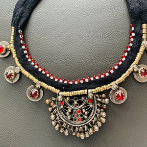 May include: A black and gold necklace with red and white beads. The necklace has a large, ornate pendant with a red stone in the center.