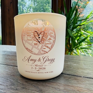May include: A matte white cylindrical candle holder featuring a rose gold circular map graphic with a heart icon. The text reads Amy & Gregg, Married, 7-3-2026, and Grand Plaza Hotel New York in a rose gold script and serif font combination.