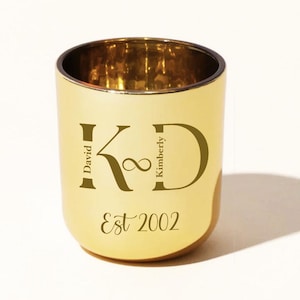 Könnte beinhalten: Ein goldfarbener Kerzenhalter mit den Initialen "KD" und den Namen "David" und "Kimberly" auf beiden Seiten. Der Text "Est 2002" befindet sich unter den Initialen. Der Kerzenhalter hat eine abgerundete Form.
