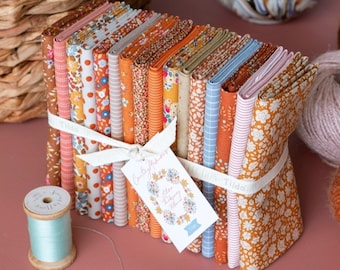 Puede incluir: Una pila de cuadrados de tela en varios colores y patrones otoñales, incluyendo naranja, marrón, crema y azul. La tela está atada con una cinta blanca y una etiqueta que dice "Cozy Autumn Fabrics".