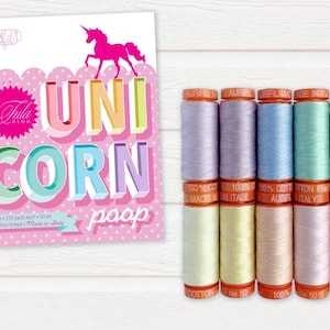 Op de afbeelding: Een set van 10 spoelen pastelkleurige katoenen draad, met het label "Aurifil" en "Made in Italy". De spoelen zijn in een rij op een wit houten oppervlak gerangschikt. De tekst "Unicorn Poop" is zichtbaar op een roze en witte kaart achter de spoelen.