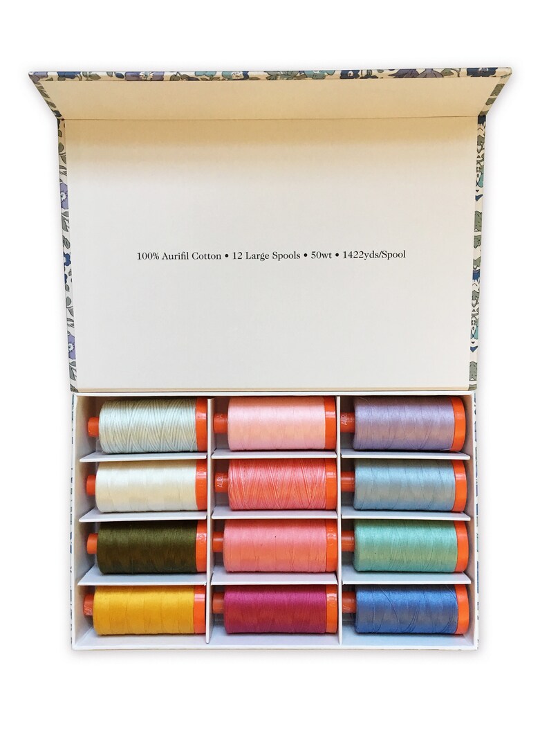 Op de afbeelding: Een doos met 12 grote spoelen 100% Aurifil katoenen garen. De spoelen zijn gerangschikt in een rasterpatroon en zijn in verschillende kleuren, waaronder blauw, groen, roze en geel. De doos is gelabeld "100% Aurifil Cotton &bull; 12 Large Spools &bull; 50wt &bull; 1422yds/spool".