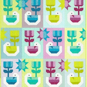 Può includere: Un blocco di trapunta con un motivo ripetitivo di fiori stilizzati in vasi con uccelli. I fiori sono in tonalità di blu, verde, giallo e rosa. Gli uccelli sono bianchi con accenti blu, verdi, gialli e rosa. Lo sfondo è di colore giallo chiaro, blu chiaro e rosa chiaro.